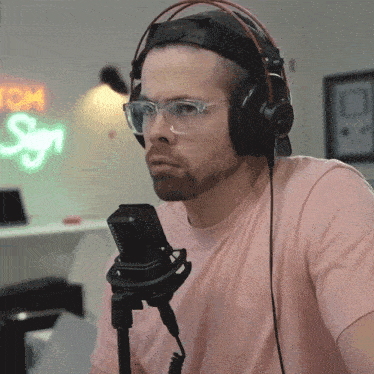 a man wearing headphones and glasses is sitting in front of a neon sign that says tom sign