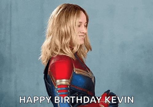 captain marvel is wearing a red , blue and gold superhero suit and smiling .