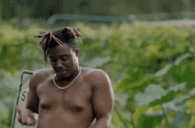 a shirtless man is sitting in a chair in a field with his hands in his pockets .