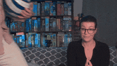 a woman sitting on a couch in front of a shelf full of board games including one called sherlock