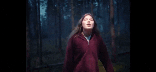 a woman is screaming in the woods with her mouth open .