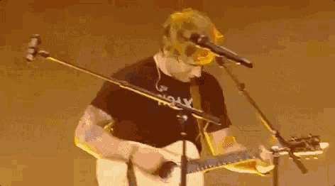 a man is playing an acoustic guitar and singing into a microphone on a stage .