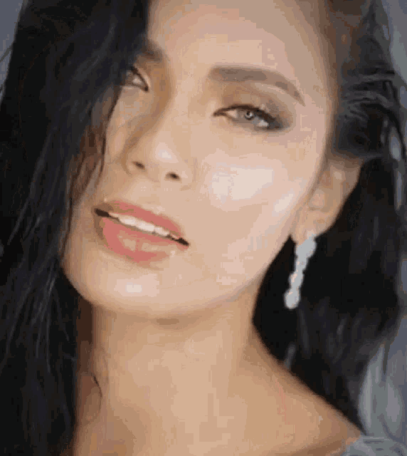 a close up of a woman 's face with long black hair and earrings looking at the camera .