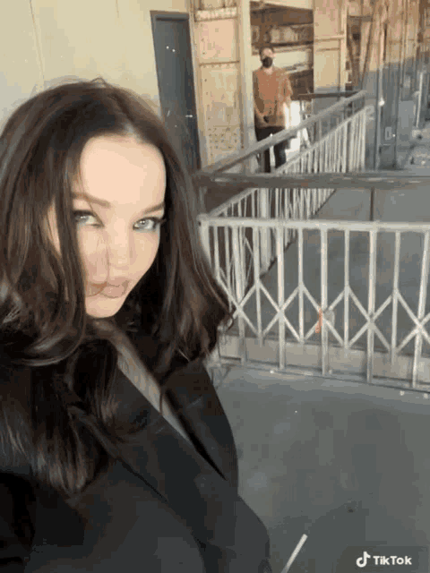 a woman is standing in front of a fence with a tiktok logo on the bottom right