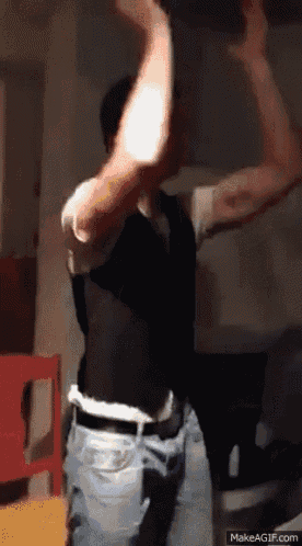 a man in a vest and jeans is dancing with his arms in the air on make a gif.com