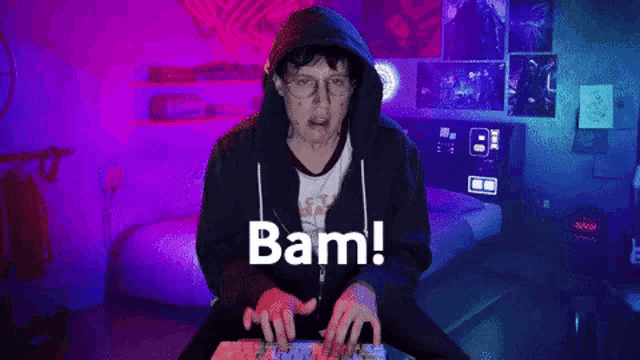a man in a hoodie is typing on a keyboard and the word bam is on the screen
