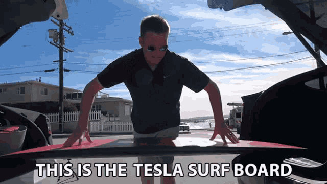 a man is holding a surfboard in the back of a tesla car