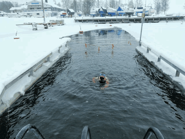 a man in a green hat is swimming in a frozen body of water