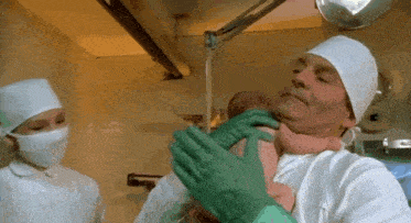 a surgeon is holding a baby in his arms while a nurse looks on .