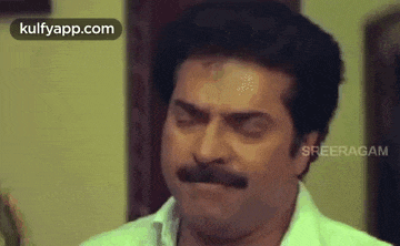 a man with a mustache is making a funny face while sitting in a room .