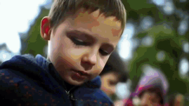 a young boy in a blue jacket looks down at something