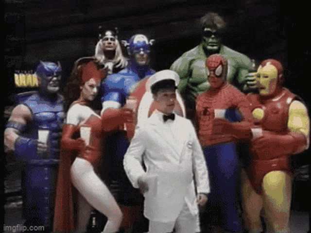 a man in a white suit is standing in front of a group of superheroes