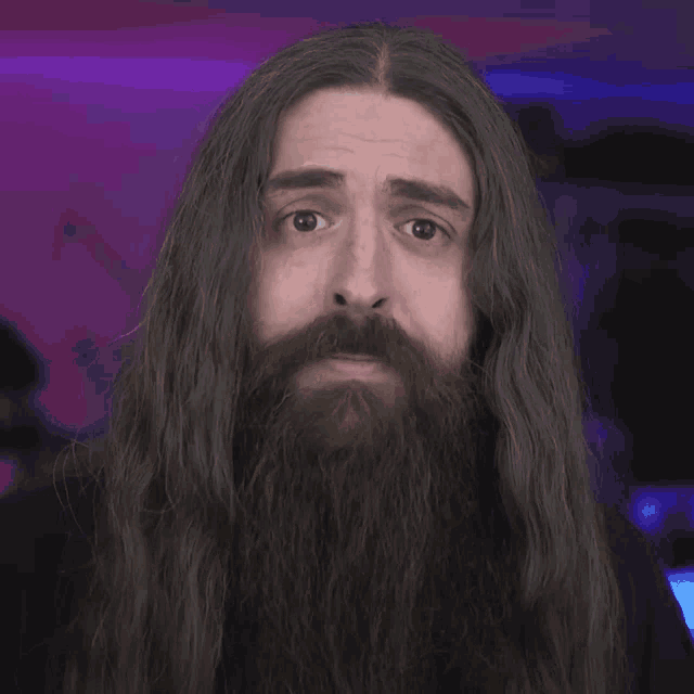 a man with long hair and a beard smiles at the camera