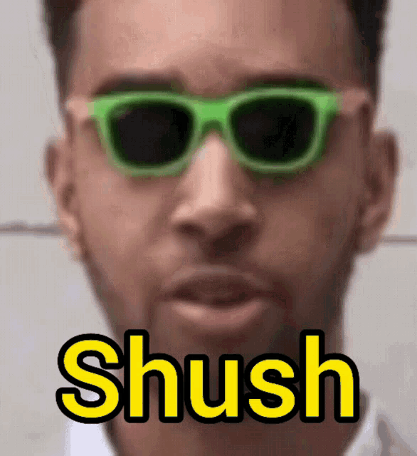 a man wearing green sunglasses says shush in yellow