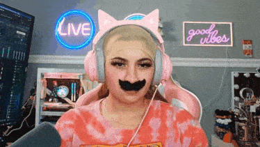 a woman wearing headphones and a fake mustache in front of a sign that says live and good vibes