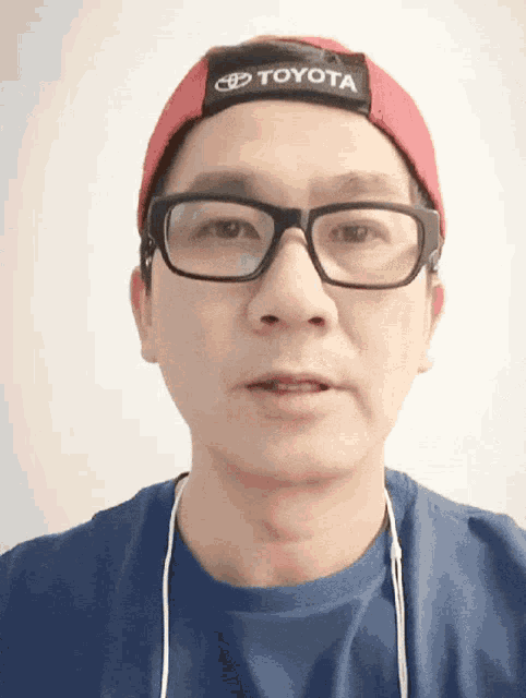 a man wearing a toyota hat and glasses looks at the camera