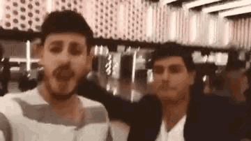 two men are standing next to each other in a crowded room and making funny faces .