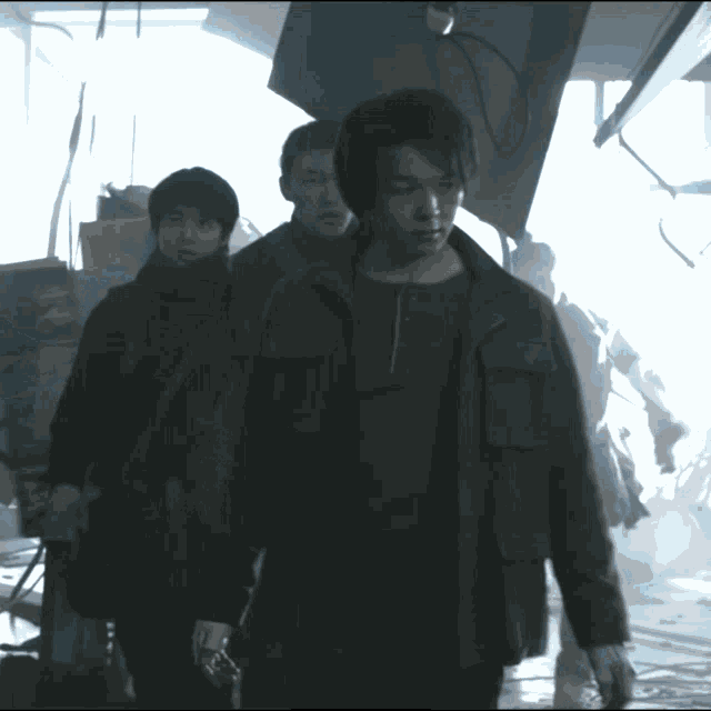a man in a brown jacket is walking with two other men in a dark room