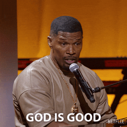 a man singing into a microphone with the words god is good written above him