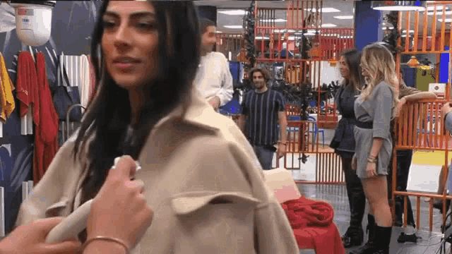 a woman is trying on a coat in a store while a group of people are standing around her .