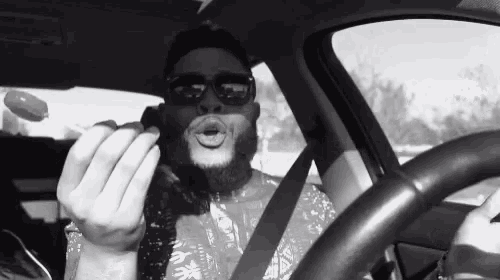 a man with a beard and sunglasses is driving a car .