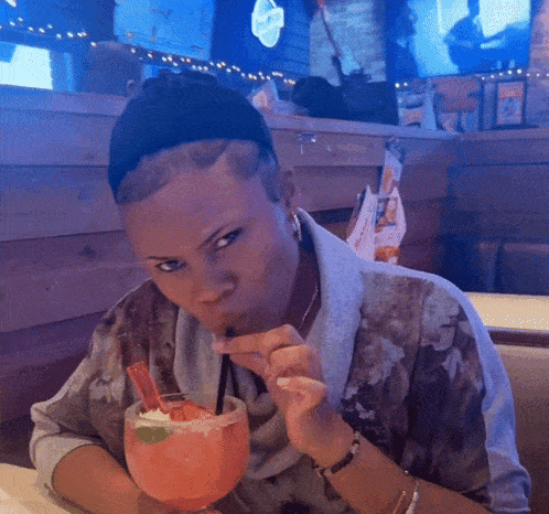 a woman sitting at a table drinking from a glass with a straw