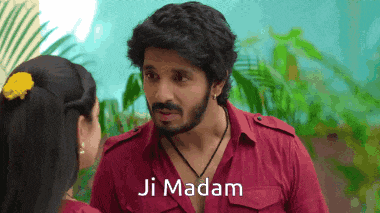 a man in a red shirt is talking to a woman with ji madam written on the bottom