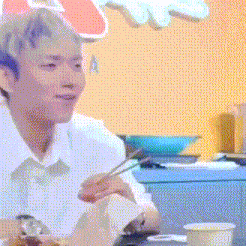 a young man is sitting at a table with chopsticks in his hand .