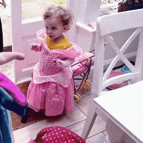 a little girl dressed in a pink dress is standing next to a doll stroller