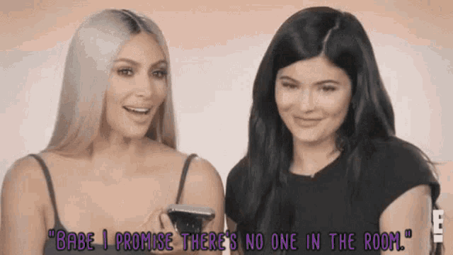 two women are standing next to each other and one of them is holding a cell phone .