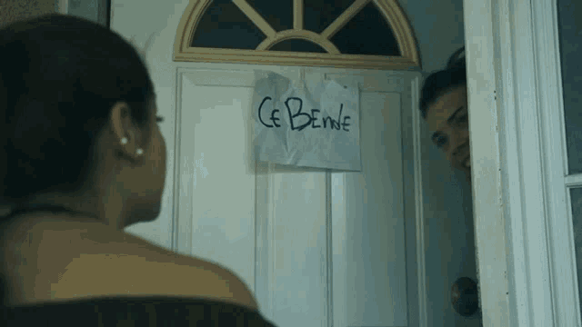 a woman stands in front of a door that has a sign on it that says ce benne