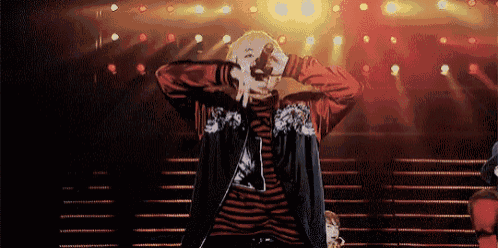 a man in a red jacket is dancing on a stage with a microphone .