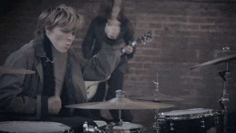 a man playing drums while another man plays a guitar