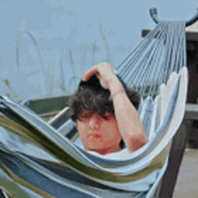 a young man is laying in a hammock holding his hair .