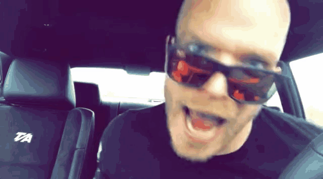 a man wearing sunglasses and a black shirt with the letter r on the back seat