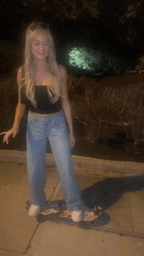 a blonde woman is riding a skateboard on a sidewalk at night
