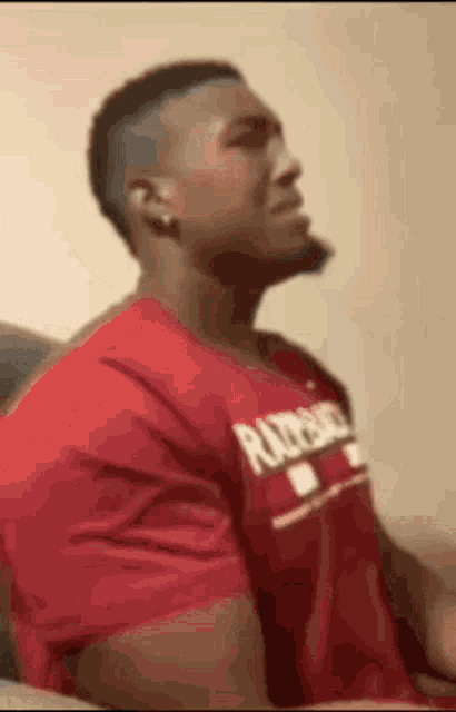 a man in a red shirt is sitting on a couch with his head down .