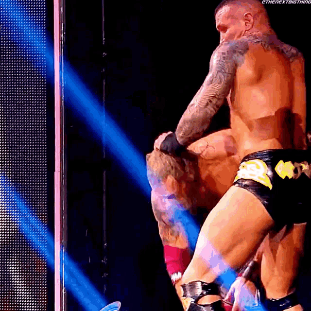 a wrestler with a tattoo on his back is holding another wrestler
