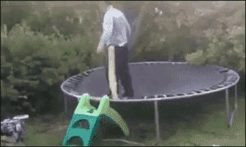 a man is standing on top of a trampoline next to a green slide .
