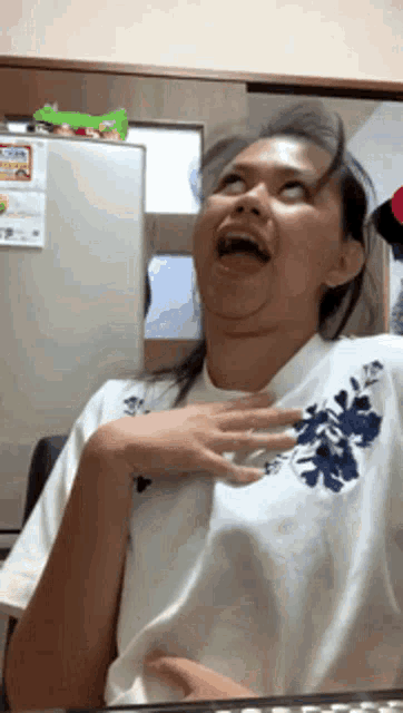 a woman wearing a white shirt with blue flowers on the chest is making a funny face