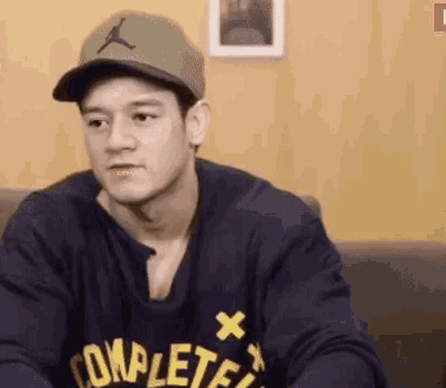 a young man wearing a hat and a sweatshirt is sitting on a couch .