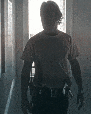 a man in a white t-shirt and black pants is standing in a hallway with a gun in his belt .