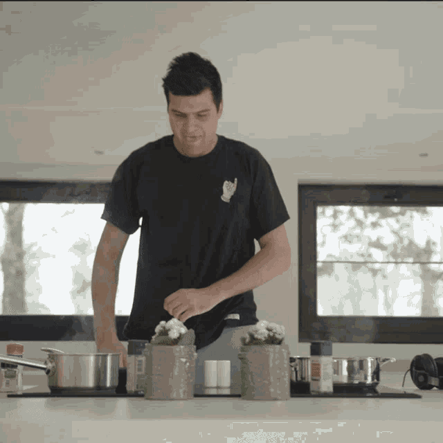 a man in a black t-shirt with a hand on the back is cooking in a kitchen