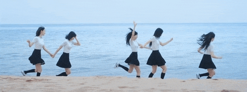 a group of girls are holding hands and running on the beach