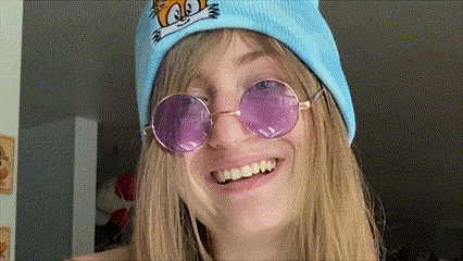 a woman wearing a blue hat and purple sunglasses smiles for the camera