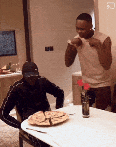 two men sitting at a table with a plate of pizza on it