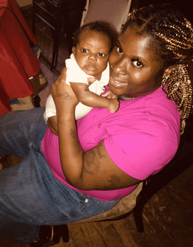 a woman in a pink shirt is holding a baby and has a tattoo on her arm that says " i love you "