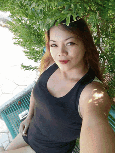 a woman in a black tank top takes a selfie in front of a tree