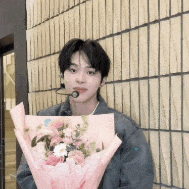 a man holding a bouquet of flowers in front of a brick wall