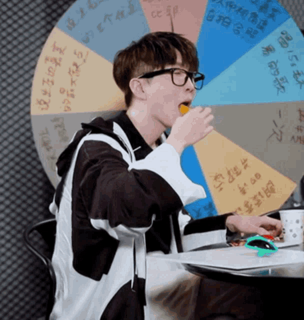 a man with glasses is eating an orange in front of a wheel with chinese writing